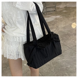 Detail of black pleated nylon tote bag featuring decorative bows on the shoulder straps