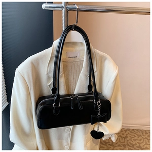 Detail of black baguette bag featuring silver zippers and a metal heart bow pendant