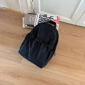 Top view of a black nylon backpack with drawstring pockets on a light wood background
