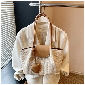 Close-up of woven herringbone straw tote with brown leather handles and heart charm