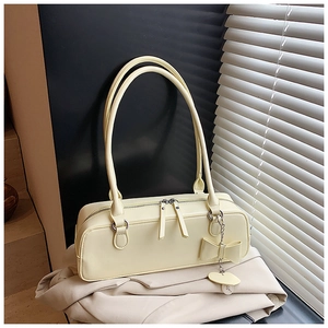 Detail of cream baguette bag with dual zippers and decorative bow heart pendant
