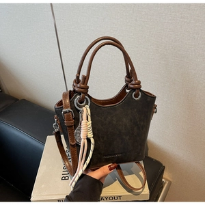 Détails d'un sac seau vintage montrant les poignées brunes, la bandoulière et les boucles
