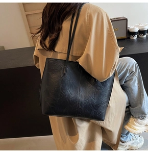 Detailed view of black pleated leather tote bag worn with a khaki trench coat