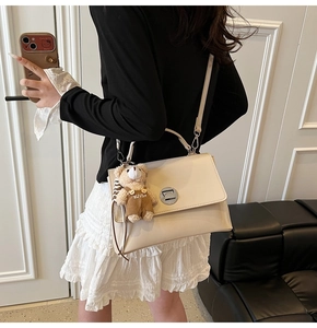 Detail of cream flap handbag with silver twist lock and cute bear doll charm attached