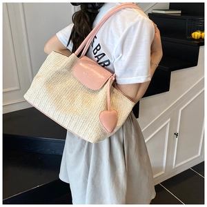 Detail of beige straw tote bag with pink leather flap and heart pendant ornament
