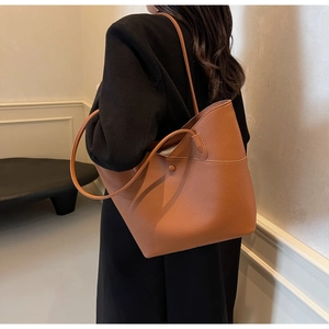 Side view of a brown lychee pattern leather tote bag worn by a model in a modern room