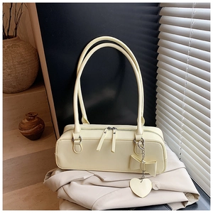 Detail of light yellow baguette bag with bow charm on a beige blazer background