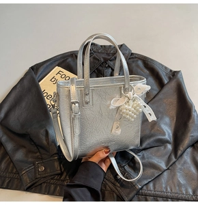 Détail du sac cabas argenté métallisé avec pendentif en dentelle blanche et perles