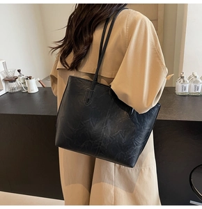 Detail of vintage black leather tote bag with long straps worn on shoulder by model