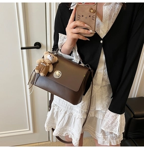 Detail view of a vintage dark brown square bag with a silver buckle and plush bear charm