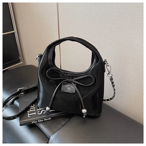 Détail d'un sac à main en cuir verni noir avec un nœud fin et une bandoulière chic