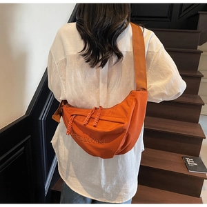 Detailed view of an orange crescent crossbody bag featuring embroidery and a woven puller