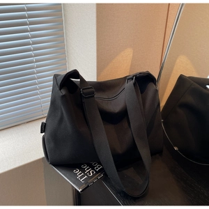 Detailed macro shot of a black canvas tote bag with side label and adjustable shoulder strap