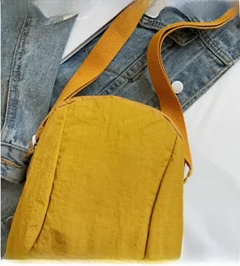Détail d'un sac bandoulière en nylon jaune avec fermeture éclair et logo QIHUANMAO