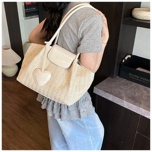 Detail of a beige woven tote bag featuring creamy white leather straps and heart pendant