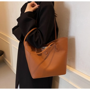 Close-up of brown lychee grain leather texture and round button detail on a tote bag