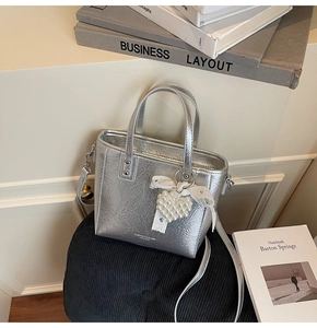 Détail du sac argenté métallisé avec pendentif perle cœur et nœud en dentelle blanche