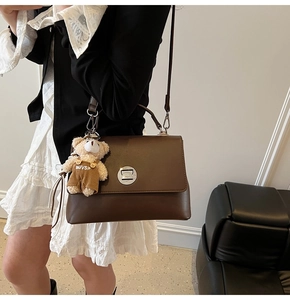 Detail of dark brown leather messenger bag featuring silver metal twist lock and bear charm