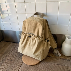 Detail of khaki nylon backpack featuring drawstring front pocket and adjustable straps