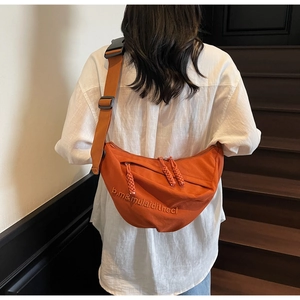 Detail of bright orange half-moon crossbody bag with embroidery on casual white shirt