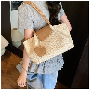 Detail view of woven straw tote bag with brown leather flap and heart pendant charm