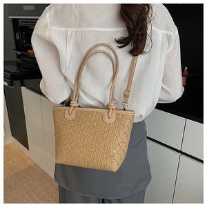 Detail of woven straw tote bag with knotted handles and adjustable crossbody strap