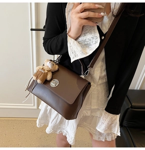 Detailed view of brown leather crossbody bag with silver twist lock and bear charm