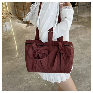 Detail view of burgundy nylon bucket bag featuring large side bow decorations and shoulder strap