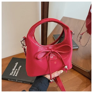 Détail du sac en cuir verni rouge avec chaîne argentée et plaque logo avec nœud