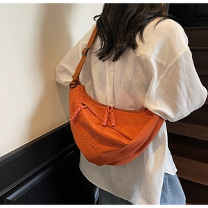 Macro detail of vibrant orange canvas dumpling bag with textured embroidery and wide strap