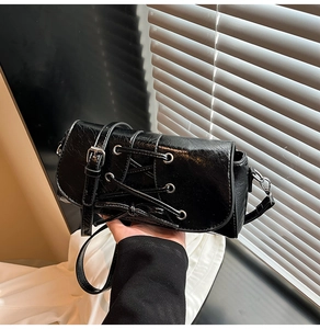 Detail of black oil-wax texture crossbody bag featuring silver buckles and lace-up design