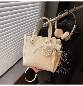 Détail du sac seau blanc crème avec un nœud en dentelle et un pendentif cœur perlé