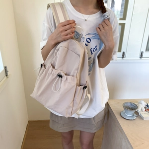 Detail view of beige nylon backpack showing drawstring side pockets with black buckles