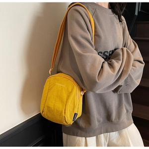 Vue latérale d'un petit sac bandoulière en nylon jaune avec broderie de lettres blanches