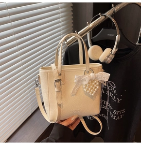 Détail d'un sac à main crème avec un pendentif en perles en forme de cœur et un nœud