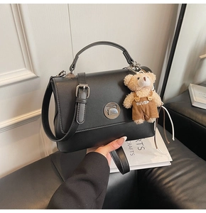Close-up of black retro handbag with silver buckle and cute plush bear charm detail