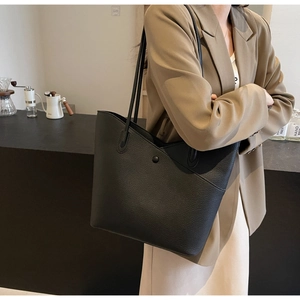 Detail view of large black leather tote bag featuring a minimalist V-shaped front pocket