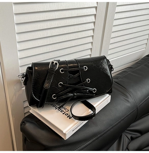Detailed view of black pleated shoulder bag with decorative lacing and silver eyelets
