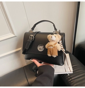 Detail view of black leather handbag featuring silver twist lock and cute teddy bear charm