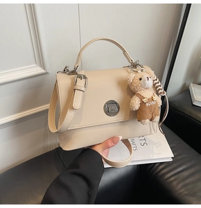 Detail of cream faux leather handbag featuring silver twist lock and cute teddy charm