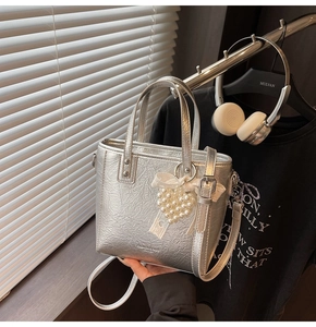 Détail du sac cabas argenté avec breloque cœur en perles et nœud décoratif en dentelle