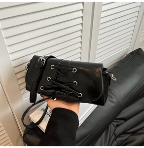 Detail of glossy black shoulder bag featuring unique lace-up design and silver eyelets