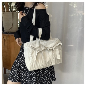 Detail of creamy white pleated nylon shoulder bag with two bows on a female model