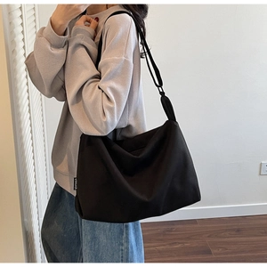 Detailed view of black canvas crossbody bag with white woven label on casual outfit