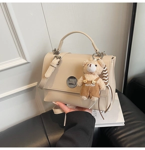 Detail view of a cream-white square handbag with a plush bear charm and metallic turn-lock