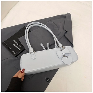 Detail of light blue baguette bag with heart charm and bow on a grey suit jacket