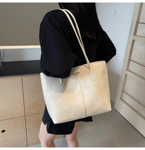 Detail of beige oversized tote bag with vintage crinkled texture on shoulder of model