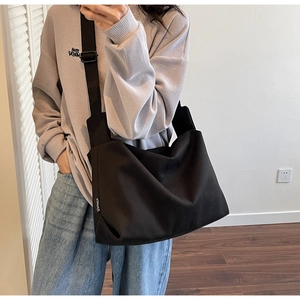 Detail of black canvas messenger bag featuring a wide nylon strap and side brand label