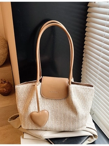 Large hand-woven straw tote bag with brown leather handles and heart charm in home setting