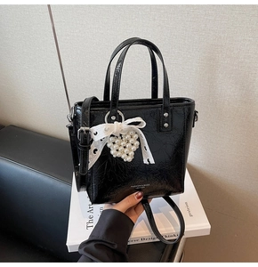 Détail du sac seau en cuir verni noir avec nœud en dentelle et breloque cœur